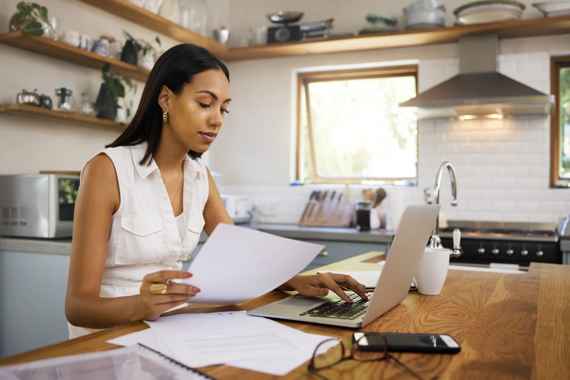 canadian-sitting-at-kitchen-table-with-laptop-and-calculator-reviewing-budget-and-savings-account-statements-to-start-building-emergency-fund