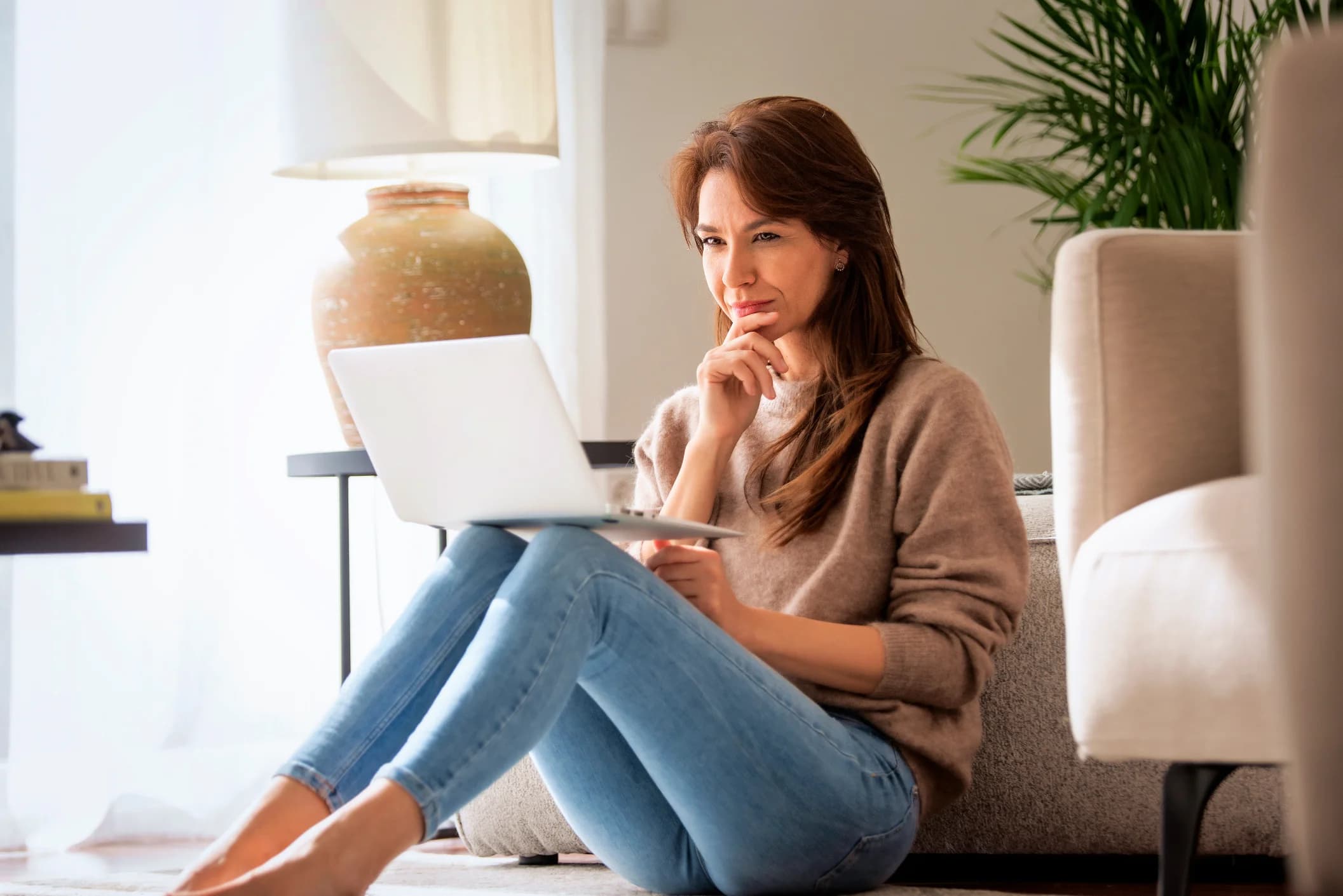Thinking woman sitting at home and using laptop