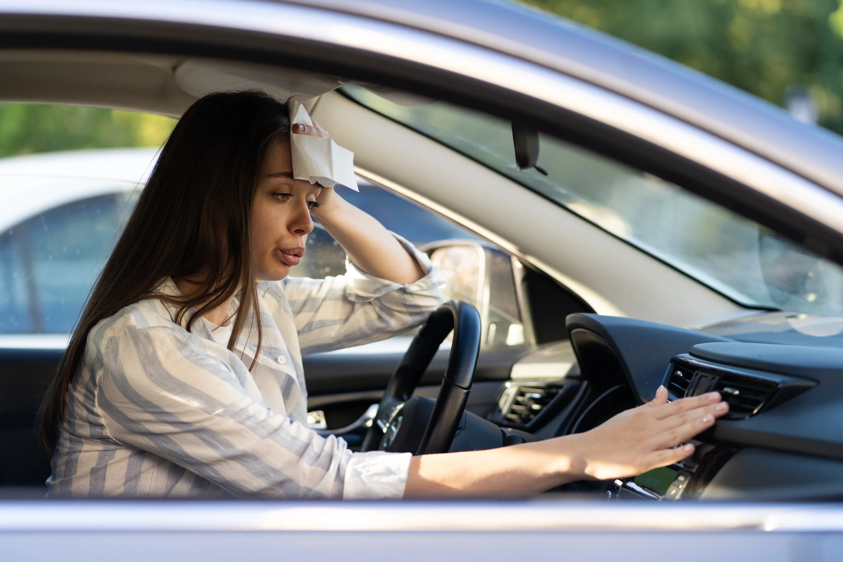 Exhausted young woman suffering from heat inside car with broken air conditioner