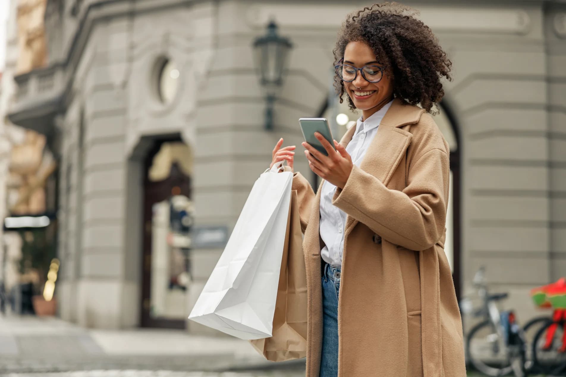 Woman after shopping with paper bags standing in city and using phone